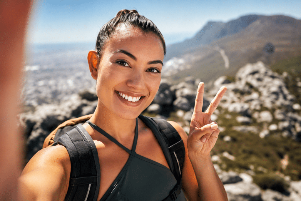 Woman posing for a photo while hiking, showing off her bright, shiny teeth from recent dental crown treatment.