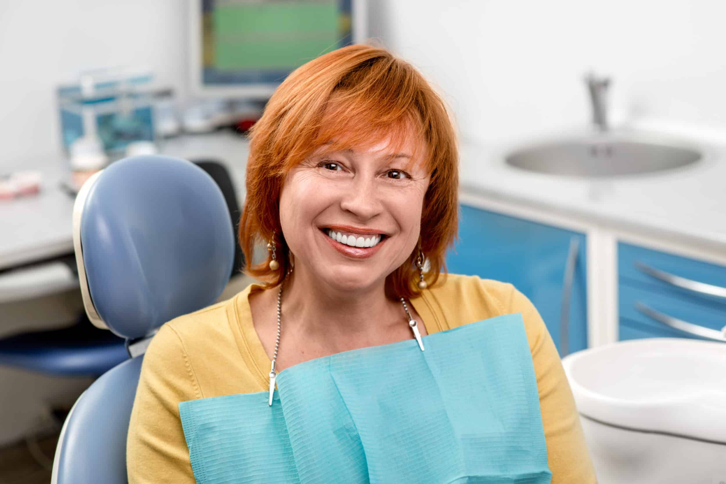 Older woman smiling brightly at the dentist's office after getting All-on-4 Dental Implants for improved oral health.
